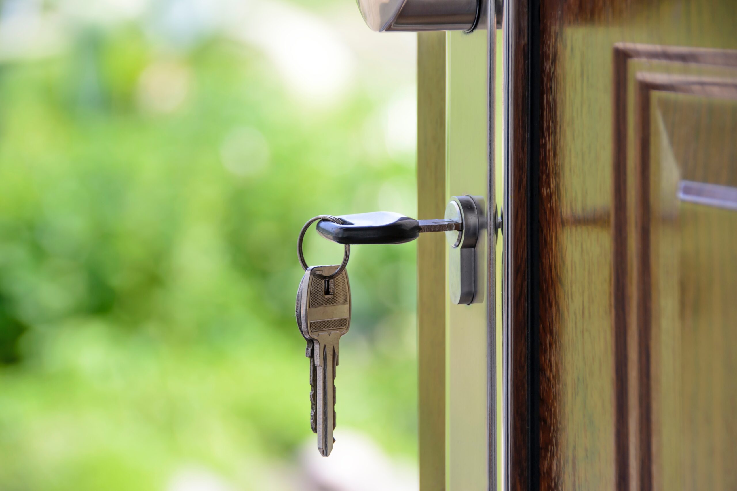 Open front door with keys in lock on a sunny day